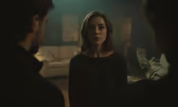 an unforiling woman stands in a dark room looking back