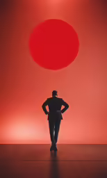 the man is standing in the dark and looking away from the red object