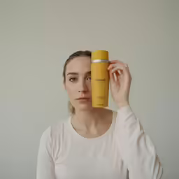 a young woman holding up a small yellow cylindrical bottle