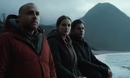 three people sitting on a beach next to the water
