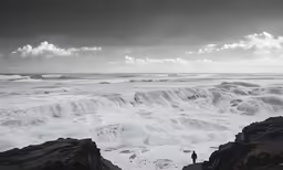 man standing on large rocks near water as storm approaches