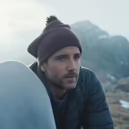 the man holds his surfboard while looking to his left