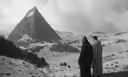 two people standing in the snow near mountains