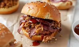 a pulled pork sandwich on a bun with a cup of tomato sauce