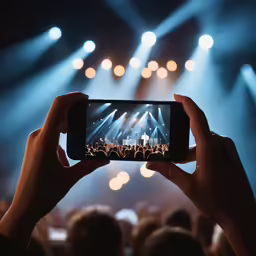 person holding up a smart phone with the concert being viewed from behind them