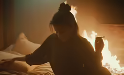 a woman holding a cigarette in one hand while sitting on a bed