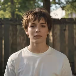 a young man wearing a white shirt stares at the camera