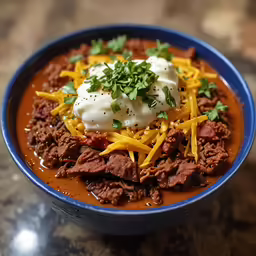 beef and potatoes in a chili soup is garnished with sour cream