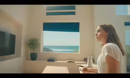 a woman standing in front of a window looking out at the ocean