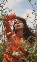 a woman wearing an orange shirt and a hat standing in a field