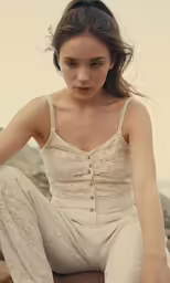 young girl wearing white clothing sitting by rocks
