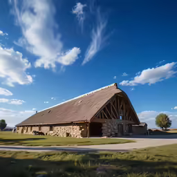 a barn with a large long roof with a tall grass area behind it