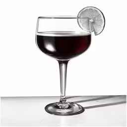 a glass of red wine on a table with a grape slice
