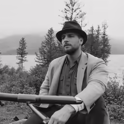 black and white image of man in suit sitting on bench with fishing rod