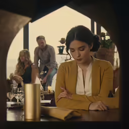 a woman in a tan jacket looking at her hand near a table