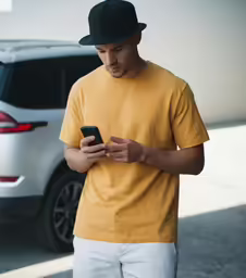 a man wearing a hat texting on his phone