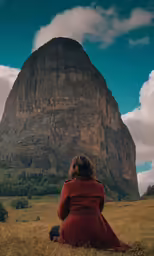 a woman sitting in the grass looking at a mountain