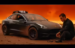 a man sitting on the ground next to a black car
