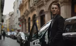 a man in black suit posing next to his vehicle