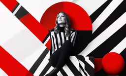 woman in striped top and black pants sitting on large red and black wall