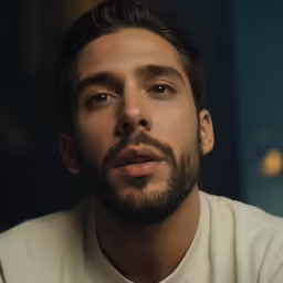 a bearded man wearing a white shirt with his eyes open