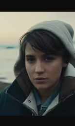 a woman stands by the water in a hooded jacket