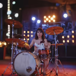 a woman is playing with drums in front of lights
