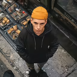 a man wearing a hat and black coat standing next to another person