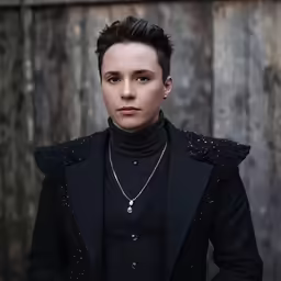 a young man standing in front of wooden wall with a necklace on his neck