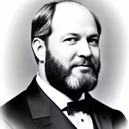 a man with a goatee and tuxedo poses in front of a white backdrop