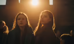 two women in black coats staring away in front of a stage