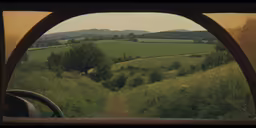 the view from the vehicle shows a dirt road, green grassy fields and hills, through an arched window