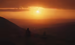 man sitting on a hill at sunset overlooking mountains