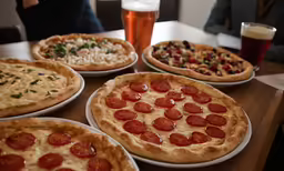 the pizzas are sitting on white plates next to a glass of beer