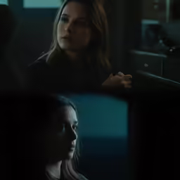two young women sit together as they watch the screen