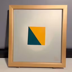 a painting made out of a yellow, blue and grey rectangle,a frame holds an abstract painting of a square, orange and green,there is a picture with an orange and blue diagonal,a frame on the wall with a painting inside,a frame with a picture hanging up against the wall