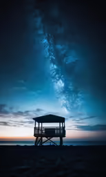 the stars and night sky above the sea and a life guard tower