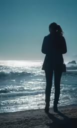 a woman in a black coat looking out at the ocean