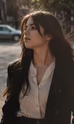a woman stands with her hair in wind, on a city street