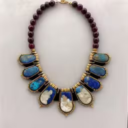 a necklace with various colored stones hanging from a necklace holder,a gold, blue and white necklace is shown,the necklace was made of blue stone and brass metal beads,a necklace that is decorated with beads and stones,a necklace that has beads on the side of it