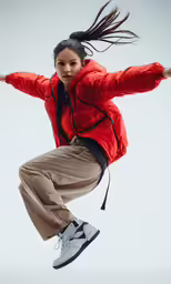 the young woman in the orange jacket is jumping