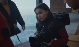 a woman is holding a camera while standing near some water