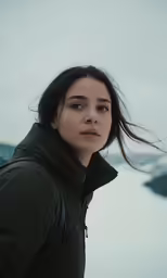 a woman in a black jacket standing in front of a snowy lake