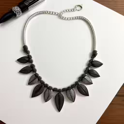a long silver necklace with metal leaves on it,a necklace sits on a table next to some scissors