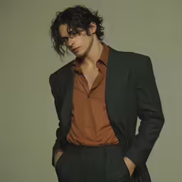 a man with curly hair standing with his hands in his pockets