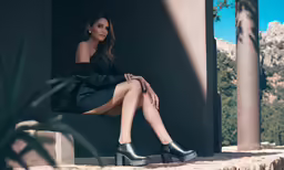 the woman in black outfit and boots is sitting on a stone wall
