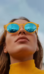 a woman wearing bright yellow sunglasses is looking up at something behind her