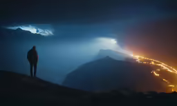 a lone man standing on top of a cliff in the mountains at night