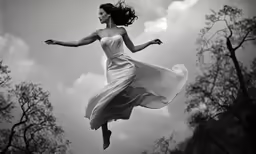 a girl in the air with her dress flowing and trees in the background