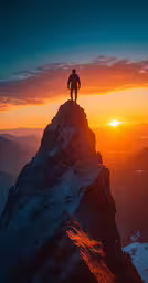 the person stands atop the peak looking over at the sunset